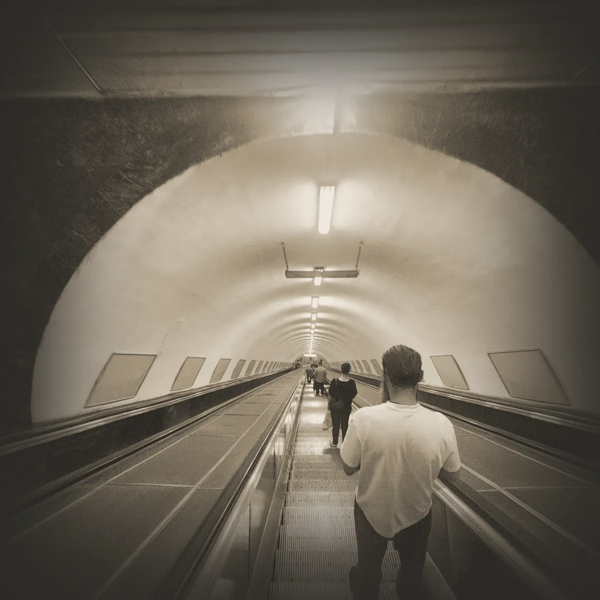 A traveler seen from behind descending a long metro escalator tunnel, Tbilisi